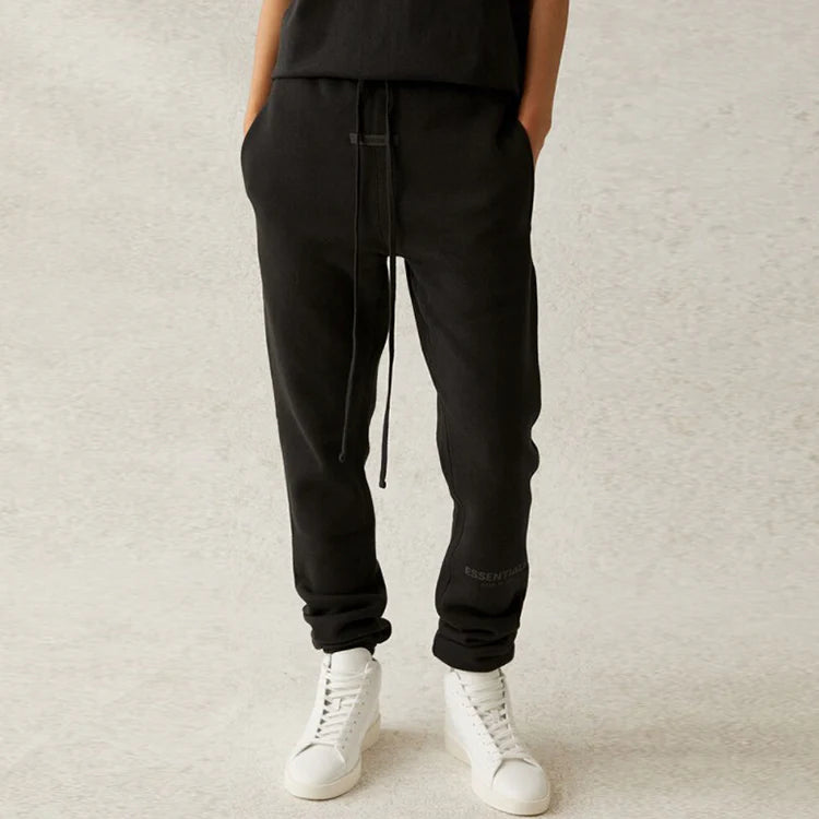 Person wearing black jogger pants and white sneakers on a light gray background